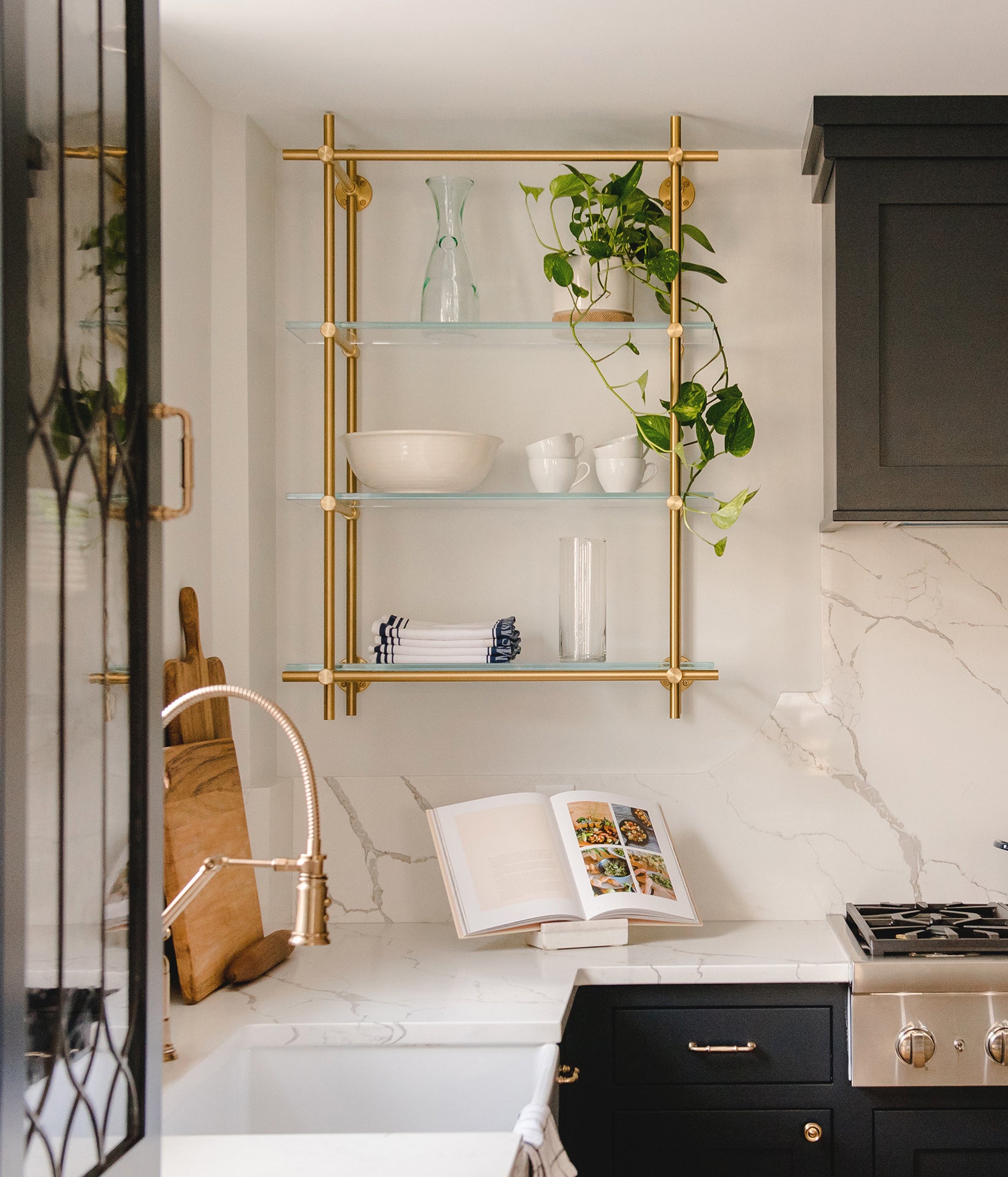 brass open shelf mounted above kitchen window with mugs and vintage lantern